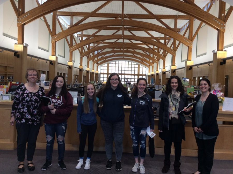 Ms. Grimmett, Jacklyne Goduti, Olivia Coy, Gretchen Mueller, Maria Wood, Ms. Milloshi, and Ms. Roberts at the circulation desk in the Abington Public Library
