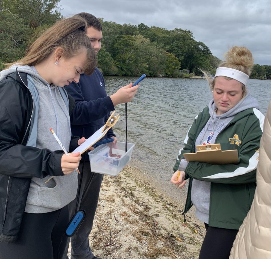 Abington High School seniors Kylie Roberts (left), Connor Whidden, and Mikayla Littman (right) test the wind speed at Mashpee Pond, Cape Cod, on an October 3, 2019 Environmental Science class field trip.