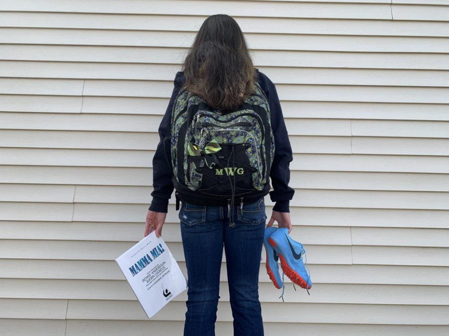 Abington High School sophomore Maria Wood holds a Mamma Mia! script, her backpack, and running spikes on March 14, 2020 as representations of cancellations due to the COVID-19 pandemic