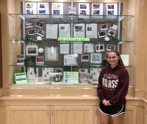 Senior Abigail Joyce poses in front of the display case containing some of the Green Wave Gazettes work in the upstairs rotunda in 2019.